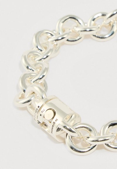 Sudraba ķēdes aproce ar lielām savienotām saitēm, gludu tekstūru un cilindrisku aizdari ar iegravētiem detaļām.