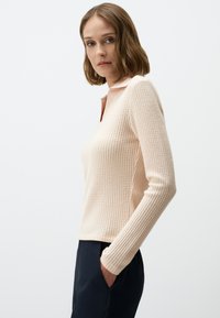 Lichtroze polo shirt met lange mouwen, voorzien van een textuurpatroon, met een kraag en geribde manchetten, gecombineerd met donkere broek.