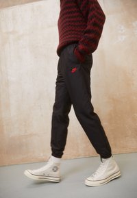 Black jogger pants with red Nike logo, elastic waistband, and tapered cuffs, paired with white high-top sneakers and a red striped sweater.