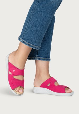Feet wearing bright pink open-toe slip-on sandals with white soles, paired with blue denim cropped pants.