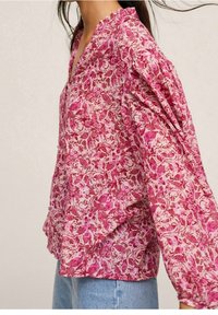 Blusa floral rosa hecha de tela ligera, con escote en V, cuello con volantes y mangas largas recogidas con un ajuste holgado.