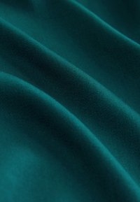 Tealfärgat tyg med en slät textur som har mjuka veck och en subtil glans. Materialet visar försiktiga vågor och ojämnheter.