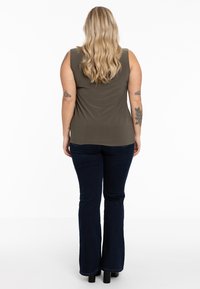 Oliven grøn ærmeløs top med en afslappet pasform, parret med mørkeblå flagrende jeans og sorte platform sko. Bølgede lyseblonde hår er synligt.