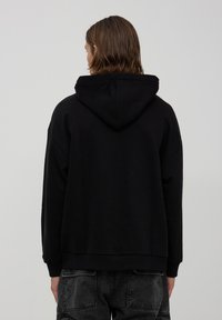Felpa nera con cappuccio, dal taglio morbido, maniche lunghe e polsini a costine. Presenta un design semplice e un tessuto morbido e testurizzato.