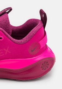 Baskets Nike en rose vif, présentant un dessus en tissu texturé, un col rembourré, un accent de marque et une semelle brillante et à motifs.