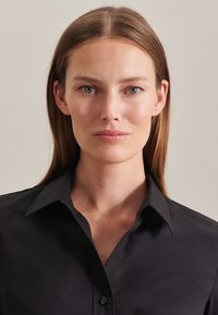 Camicia nera con colletto realizzata in tessuto morbido, dotata di bottoni e colletto strutturato. Il design è sagomato con una forma aderente.