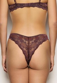 Koronkowe stringi w głębokim odcieniu burgunda, zdobione kwiatowymi wzorami i falbaniastymi krawędziami. Miękka, przezroczysta tkanina o minimalnym pokryciu tyłu.