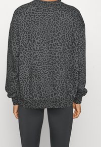 Persona viste un sudadera de manga larga gris oscuro con estampado de leopardo negro y pantalones ajustados negros, visto desde atrás.