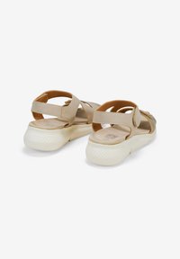 Sandali beige con cinturini incrociati, retro regolabile e suola bianca texturizzata. Materiale morbido con una finitura liscia e decorazioni minime.