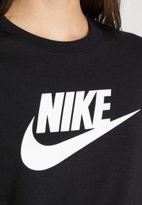 Černé bavlněné tričko s výrazným bílým logem "NIKE" a grafickým symbolem swoosh na hrudi. Kulatek výstřih a měkká textura.