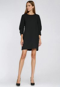 Czarna sukienka z długim rękawem i okrągłym dekoltem, z luźnymi rękawami i swobodnym krojem. Noszona z czarnymi szpilkami.