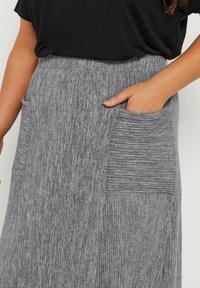 Jupe grise à côtes avec deux poches sur les côtés et de subtils plis horizontaux, associée à un haut noir à manches courtes. La texture semble douce et extensible.