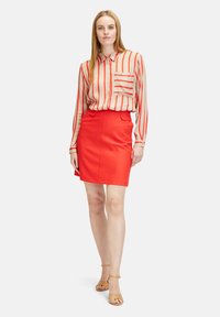 Red skirt paired with a beige and red striped blouse. The blouse has a button-up design with a single breast pocket. The outfit features smooth textures.