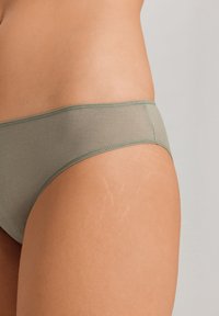 Gröna tygunderkläder med en slät textur, som har ett brett midjeband och rena sömmar längs kanterna.