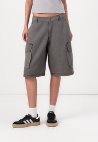 Pilki džinsai, pagaminti iš medviln�ės, su šoninėmis kišenėmis, laisvu siluetu ir kelio ilgio dizainu. Su juodais sportbačiais ir baltais kojiniais.