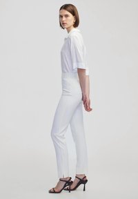 Witte kortekleding met korte mouwen, gecombineerd met witte op maat gemaakte broek met een slim fit en zijsplitten, aangevuld met zwarte hoge hakken.