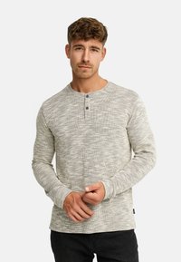 Maglietta henley a maniche lunghe in tessuto grigio strutturato con un motivo sottile, abbottonatura a due bottoni e polsini aderenti. I jeans neri completano il look.