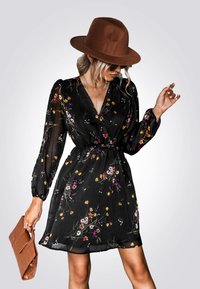 Zwarte bloemenjurk met lange,gepofte mouwen en een v-hals. Heeft een getailleerde taille en een vloeiende rok met kleurrijke wilde bloemenpatronen.