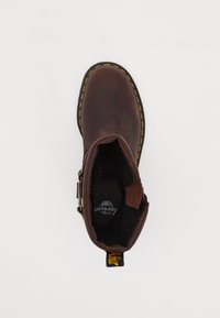 Brown leather ankle boot with yellow stitching, round toe, and a side zipper. Textured interior and logo visible inside.