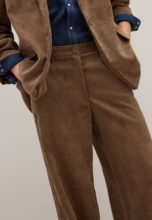 Pantalones de pana marrón hechos a medida, de pierna ancha y textura acanalada vertical. La cintura tiene cierre con botón y bolsillos laterales.