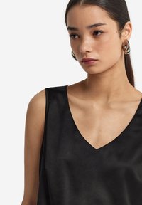 Svart ärmlös topp med V-ringning, tillverkad av ett glatt tyg, med minimala sömmar och en avslappnad passform. Discreta glänsande ytor och rena linjer.