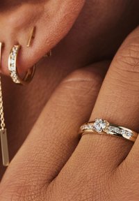 Goldcreolenohrringe mit kleinen klaren Edelsteinen, begleitet von einem goldenen Ring mit einem zentralen runden Diamanten und weiteren kleinen Diamanten am Ringband.