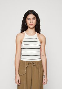 Hvit ribbet tanktop med svarte horisontale striper, utstyrt med halterneck-design. Kombinert med beige vide bukser.