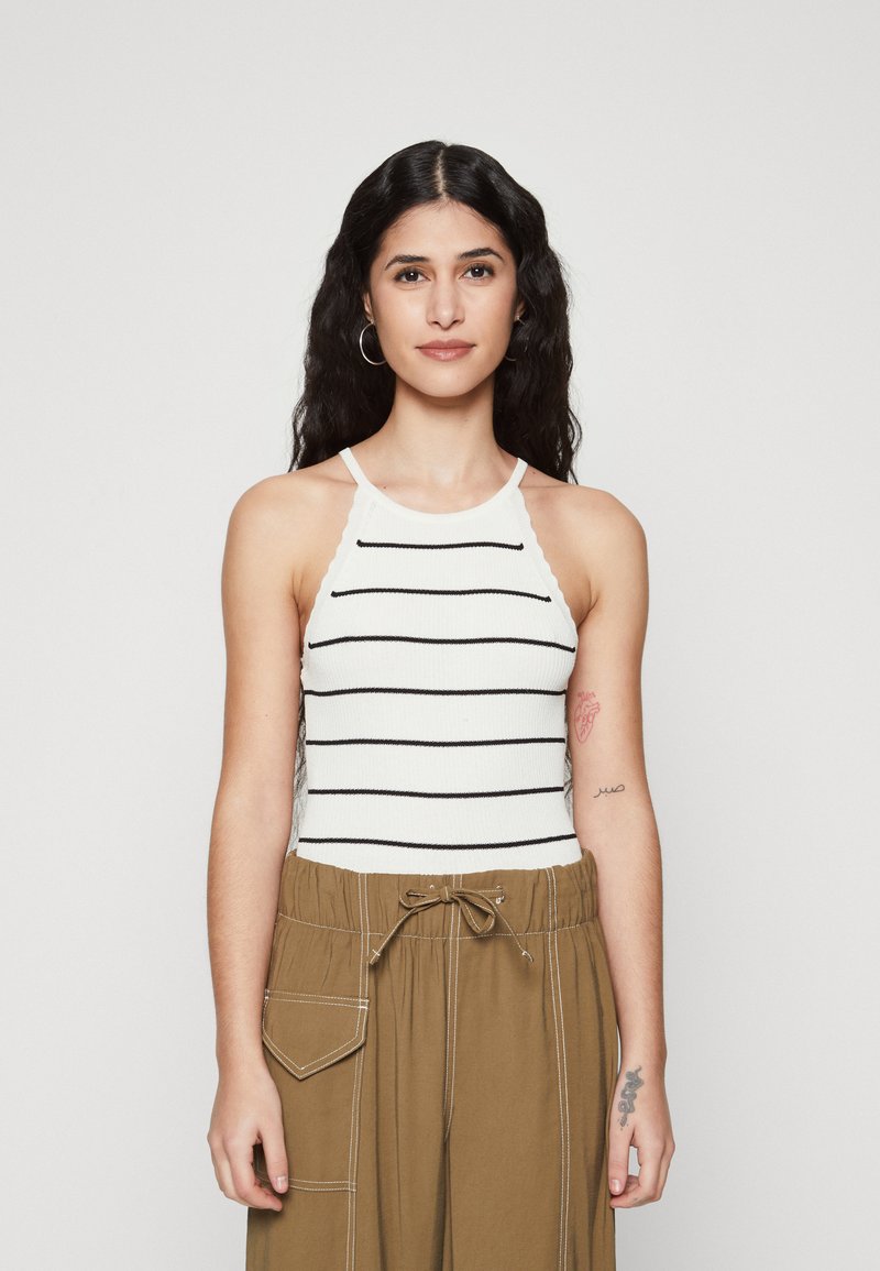 Hvit ribbet tanktop med svarte horisontale striper, utstyrt med halterneck-design. Kombinert med beige vide bukser.