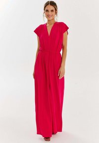 Jasnoróżowa sukienka maxi z głębokim dekoltem w kształcie litery V, krótkimi rękawami, elastyczną talią i zwiewnym materiałem, charakteryzująca się luźnym krojem i bocznymi rozcięciami.