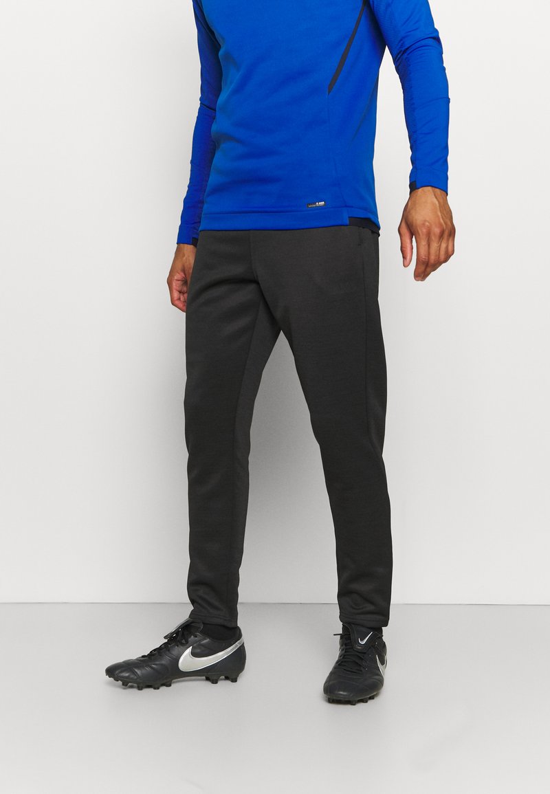 Blauw lange mouwen sporttop, zwarte accentlijnen, gecombineerd met donkergrijze tapered broek. Zwarte sportschoenen met zilveren logo en textuurdetail.