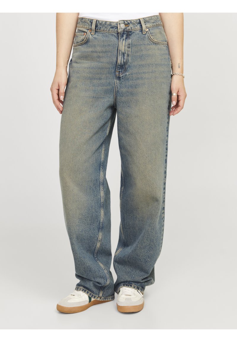 Jeans de mezclilla de tiro alto y pierna ancha en azul claro. Presentan detalles de costura y zonas desgastadas. Combinados con zapatillas blancas.