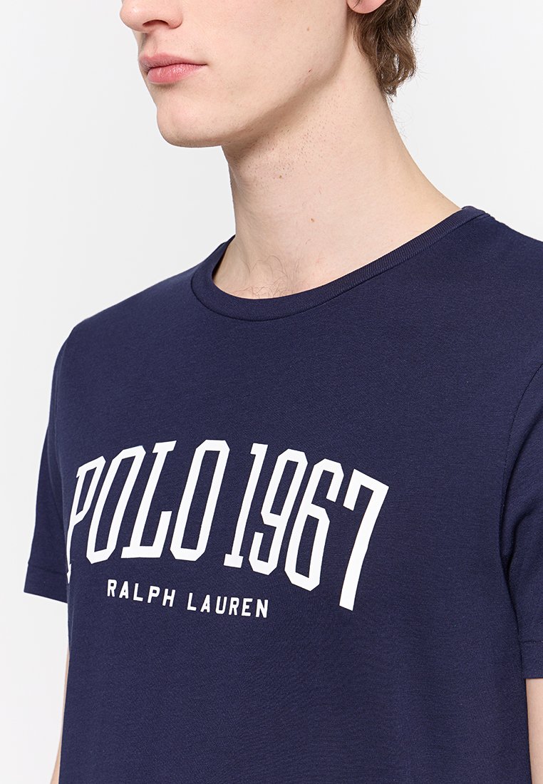 Maglietta di cotone blu navy con colletto girocollo, maniche corte e una grande stampa grafica bianca: "POLO 1967 RALPH LAUREN" sul davanti.