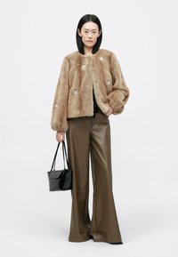 Kerged karusnahast jope heleses pruunis, kaunistatud hõbedaste tähtedega, koos kõrge vöökohaga pruunide kunstnahkpükstega ja musta käekotiga.