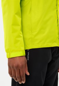 Limoengroene waterproofjack met een gladde textuur, voorzien van verstelbare manchetten en een gedeeltelijk label met de tekst "CEPLEX ACTIVE." Zwarte broek zichtbaar eronder.