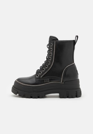 Botas de cuero negras hasta el tobillo con suela de goma gruesa, con cordones en la parte delantera, cremallera lateral y acentos de cremallera plateados.