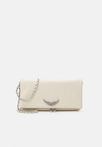 Krēmkrāsas ādas somiņa ar sudraba ķēdes siksnu, dekorēta ar spārnu aksesuāru un gludu tekstūru. Augšpusē rāvējslēdzēja aizdare.