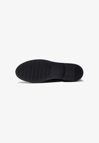 Black shoe sole with a smooth finish, featuring horizontal grooves for traction and circular accents near the heel.