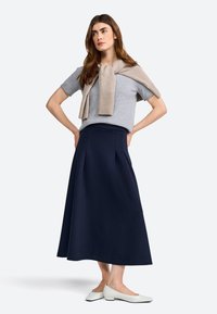 Suéter gris de manga corta con una bufanda beige caída sobre los hombros, combinado con una falda larga de color marino y zapatos blancos de tacón bajo.
