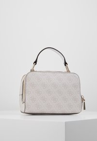 Sac à main rectangulaire beige avec un motif de logo répétitif, poignées courtes noir et blanc, et des détails en zip doré sur une surface blanche.