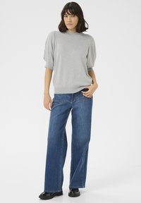 Pull gris clair avec des manches ballons courtes, associé à un jean en denim bleu à jambes larges. Des chaussures noires brillantes complètent la tenue.