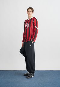 Röd- och svartrandig långärmad topp med en rund logotyp, kombinerad med lösa svarta byxor och svarta sneakers. Enkel design, sportig stil.