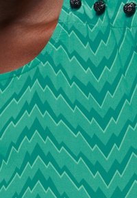 Green fabric top featuring a zigzag pattern in lighter green, round neckline, and decorative black beads at the shoulder seam.