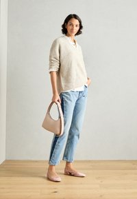 Μπεζ πλεκτό πουλόβερ, λευκό πουκάμισο από κάτω, ανοιχτό μπλε τζιν, ροζ εσπαντρίγιες και ανοιχτό ροζ τσάντα με καμπυλωτή λαβή.