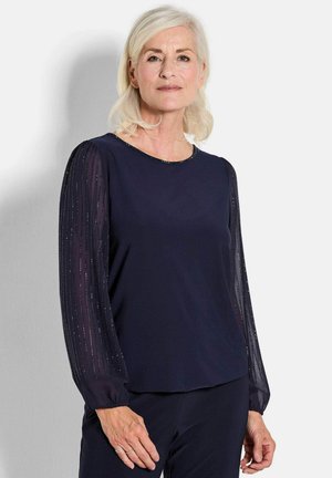Marineblaue Bluse mit langen Ärmeln, transparenten, plissierten Ärmeln und dezenten Verzierungen. Rundhalsausschnitt und lässige Passform. Weicher, glatter Stoff.