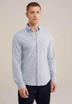 Camisa de botones azul claro con mangas largas, un cuello abotonado y una textura sutil. Cuenta con botones blancos y un dobladillo curvado.