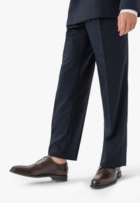 Pantaloni a righe blu navy abbinati a scarpe stringate in pelle marrone. Le scarpe presentano una punta arrotondata e un tacco basso, con finitura liscia e dettagli di cucitura.