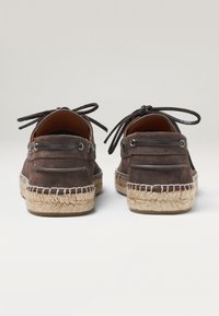 Zapatos de ante marrón con suela de yute trenzado y cordones decorativos. Presentan un forro interior suave y acentos metálicos cerca de los ojales.