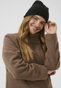Abrigo de mezcla de lana marrón con cuello alto y mangas anchas, acompañado de un gorro de punto negro. Textura suave, corte relajado, tono cálido.