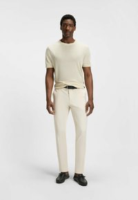 Maglione a maglia corto e a maniche corte color crema abbinato a pantaloni slim-fit beige chiaro e scarpe nere, caratterizzato da un design semplice e una texture liscia.