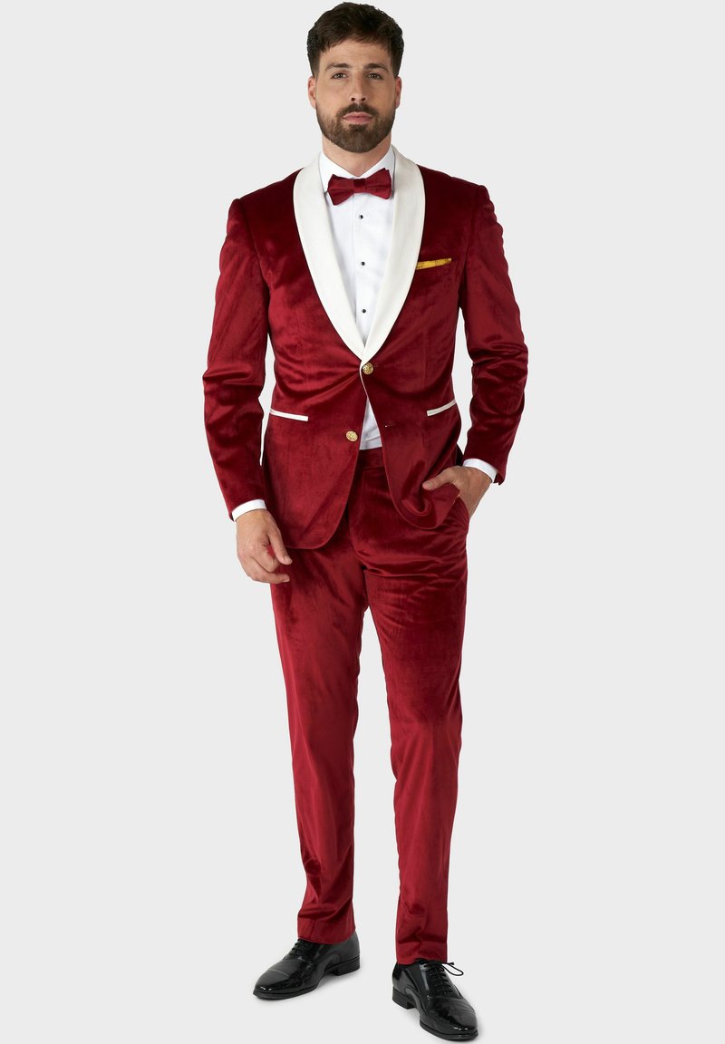 Roter Samttuxedosakko mit weißem Schalkragen, schwarzer Fliege, goldener Einstecktuch und glänzenden schwarzen Abend Schuhen. Maßgeschneiderte Passform und Knopf-Details.